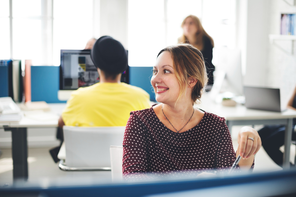 Collaboratrice souriante échangeant avec un collègue en open space, illustrant la connivence culturelle dans la relation client